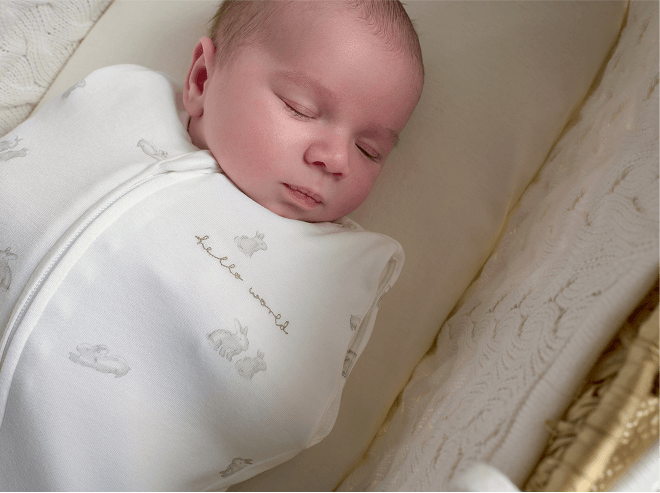 Baby sleeping in moses basket wearing bunny style swaddle
