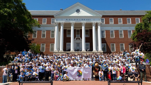 Testudo and crowd wearing rainbow turtle shell T-shirts pose outside McKeldin Library