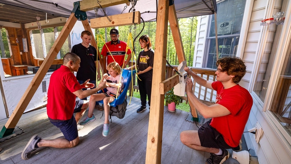 girl sits in blue swing with group of five from UMD gathered around her