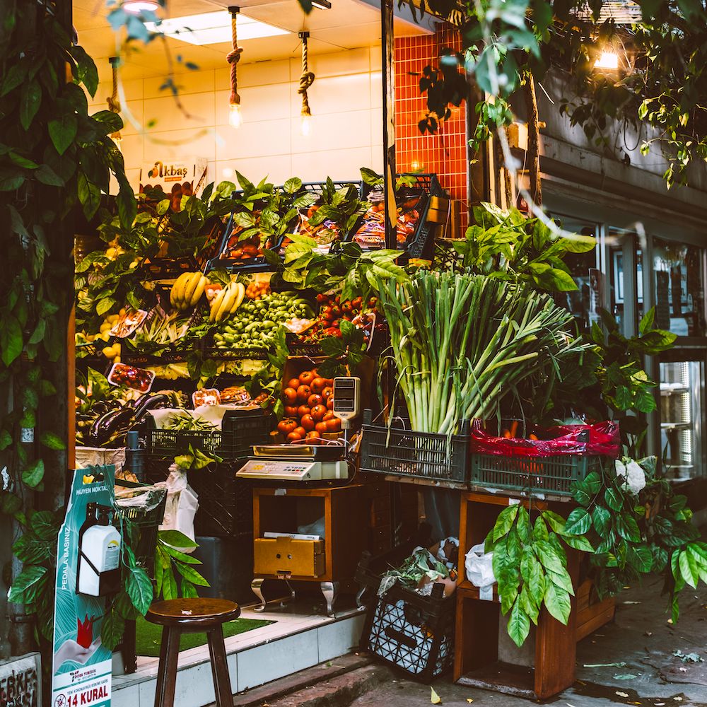 A store with its front open to the street. It is well-stocked with fruits and vegetables.