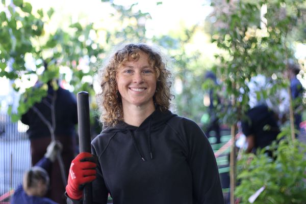 Photo: Megan Ryder, a BU student with curly blonde hair, smiling in front of greenery while holding gardening tools