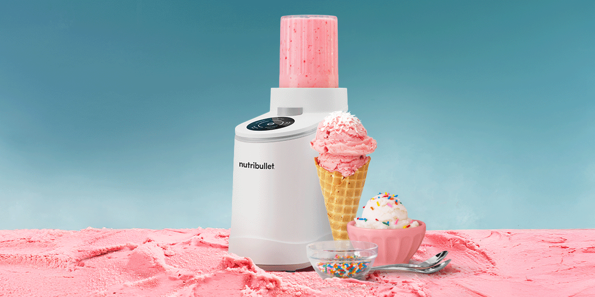 A white nutribullet cream maker sits on pink textured ice cream with a strawberry cone and sprinkle-covered sundae against a gradient blue sky.