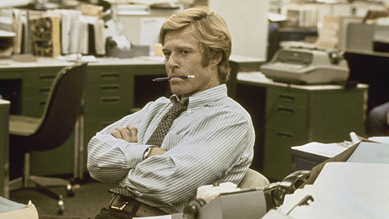  Robert Redford sits in a news room with a pencil in his mouth while playing the roll of Bob Woodward in 