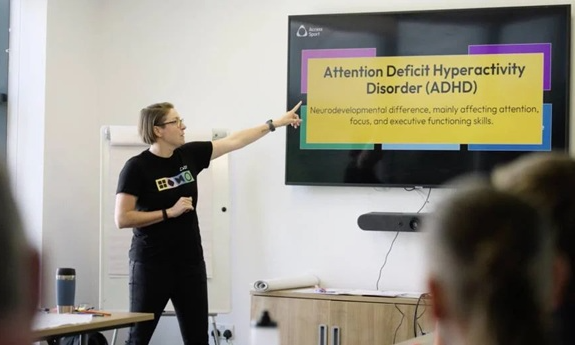 A workshop facilitator points to a screen with the title: Attention Deficit Hyperactivity Disorder (ADHD).