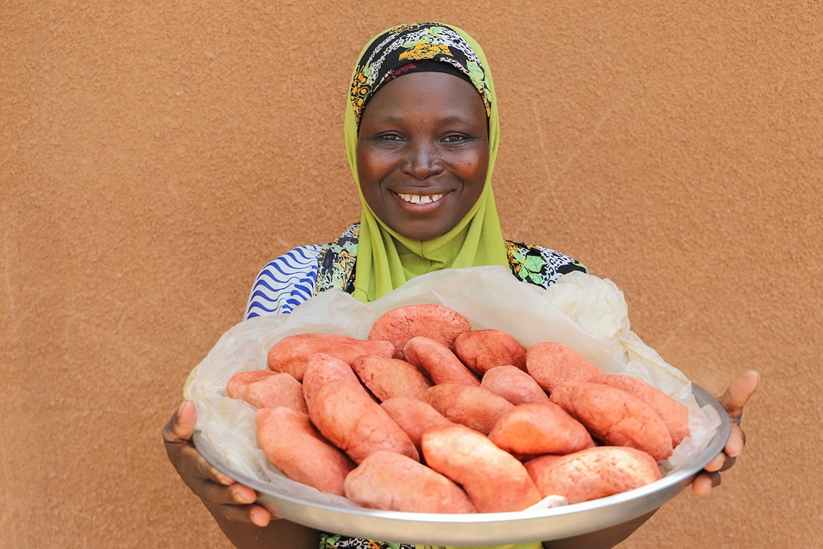 A woman holding a large tray filled with sweet potatoes