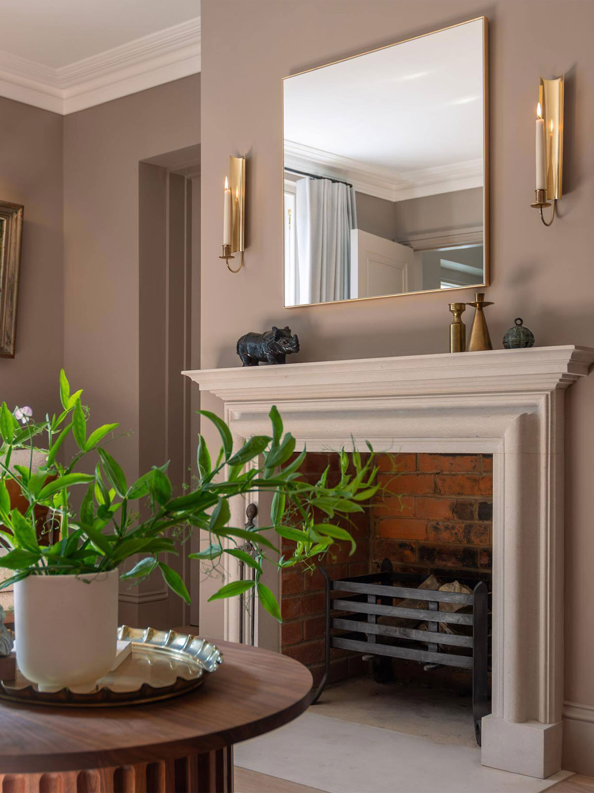 A room that seems to very gently glow. The lit candles add to the reflections from the mirror and from the burnished gold of their metal holders. The earthy wall colour is calming and grounding, the perfect foil to the black and bronze sculptures along with the soft brightness from the large green plant.