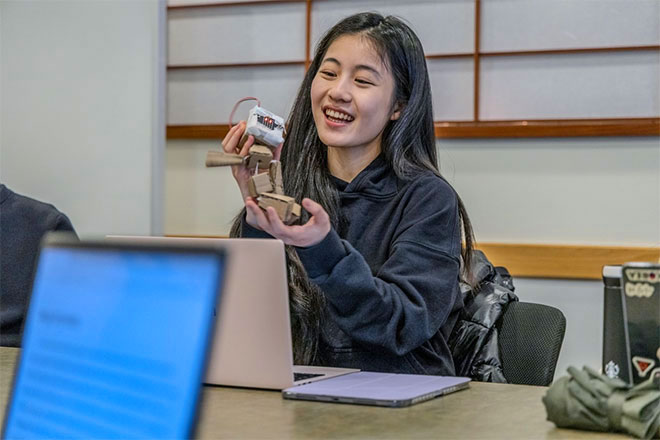 A GSE student holds a wooden construction connected to wires and batteries.