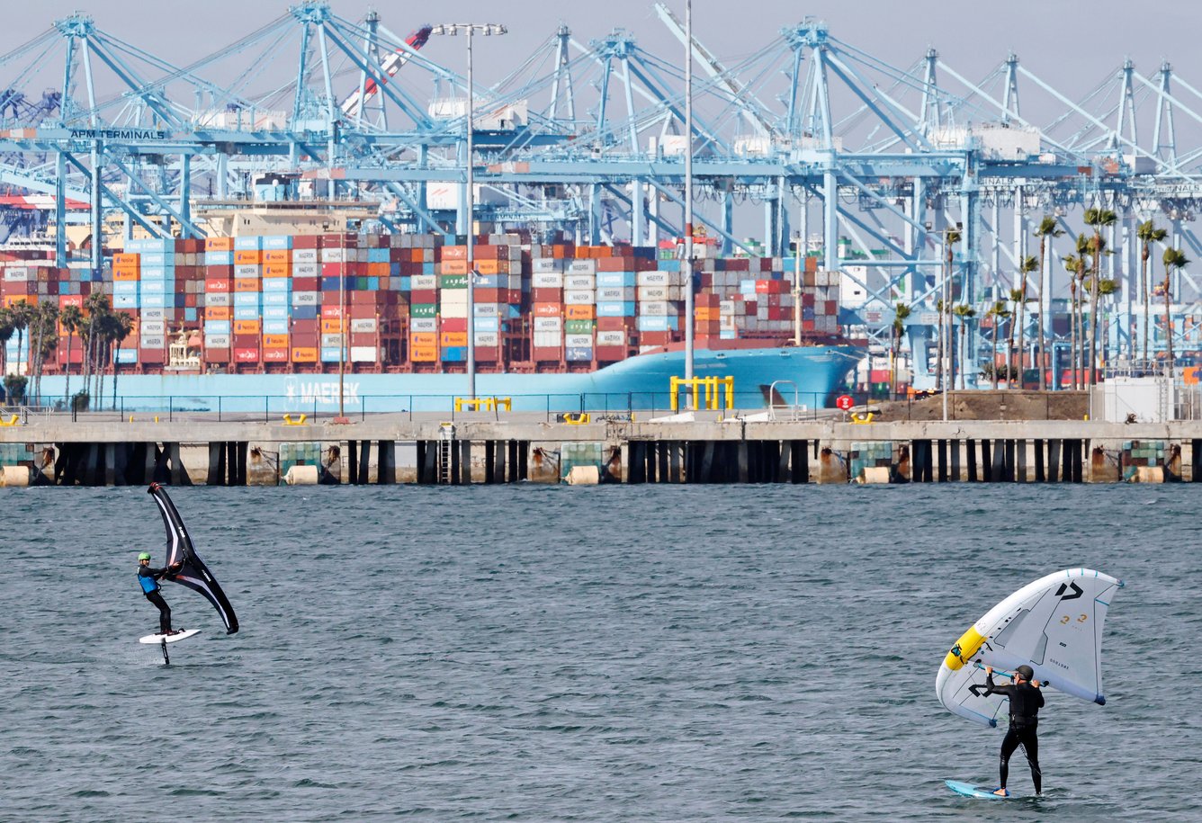 Container ship at port with windsurfers in foreground