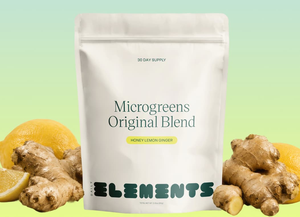 Daily Elements Microgreens Original Blend in Honey Lemon Ginger, 30 day supply, surrounded by fresh lemons and ginger