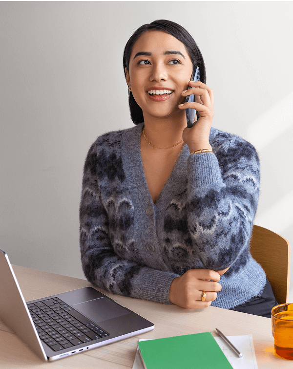 A woman working at her laptop while talking on the phone.