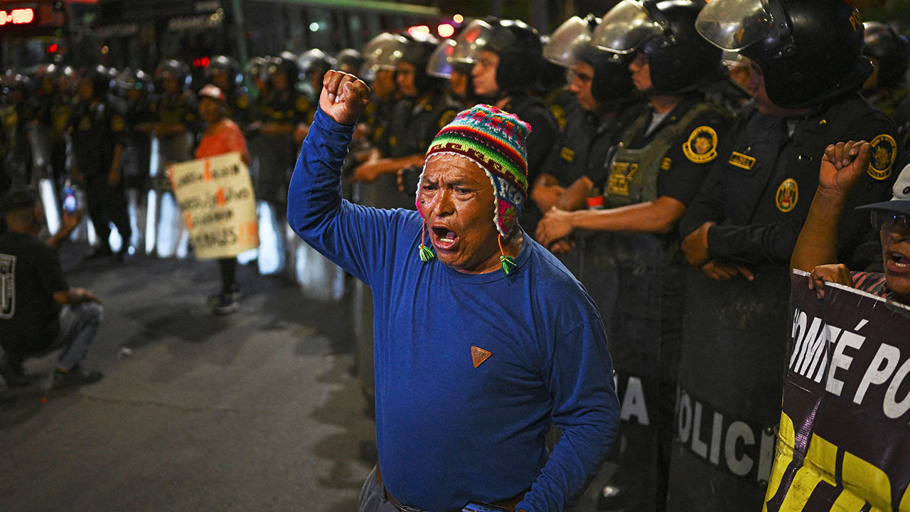 A demonstrator shouts slogans in front of a row of riot police officers