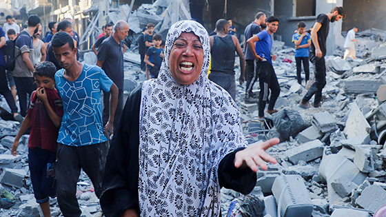 A woman gestures in agony amid the rubble of a destruction while others wander in shock.