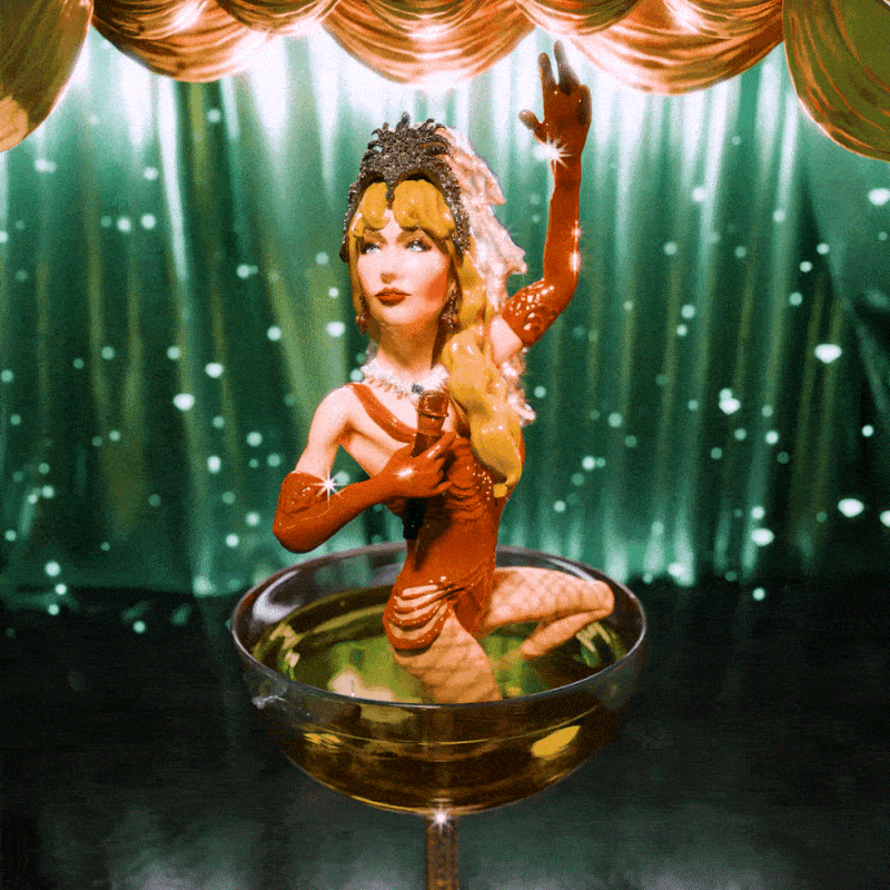 A figurine of Taylor Swift rising out of a champagne coupe on a glittering stage.