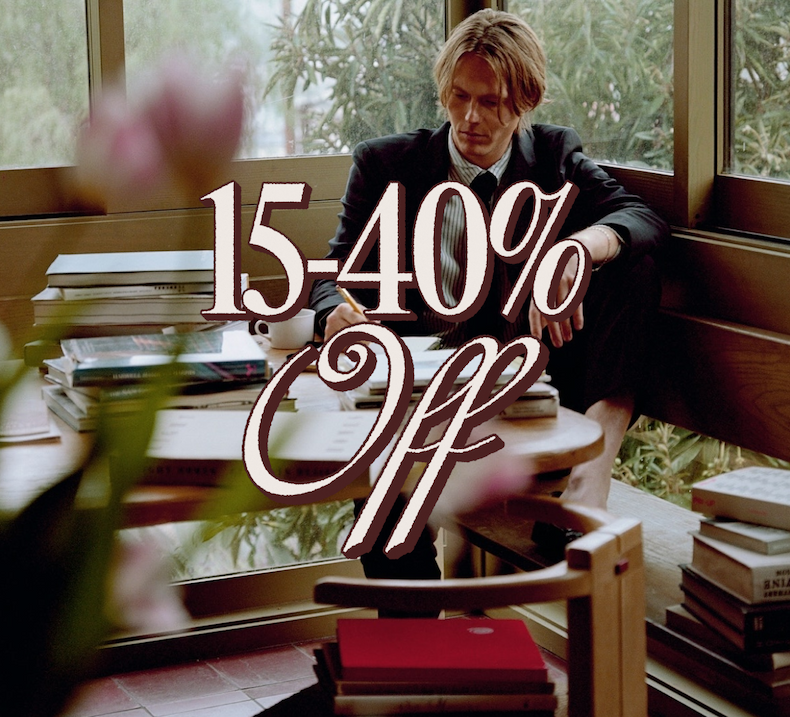 15–40% Off. Man in a suit sitting by a window surrounded by stacks of books.