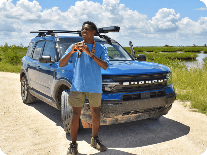 A man holding binoculars and standing in front of a parked Bronco&reg; Sport SUV