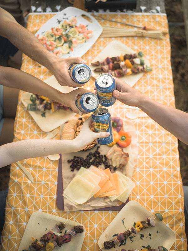 Four friends clinking cans of Summerfest Lager at an outdoor table