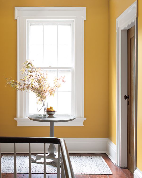 A circular table with a vase of flowers sits in a yellow painted hallway with white trim.