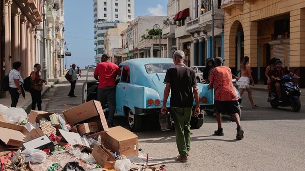 People push a broken-down, classic American car past a pile of trash in Havana, Cuba