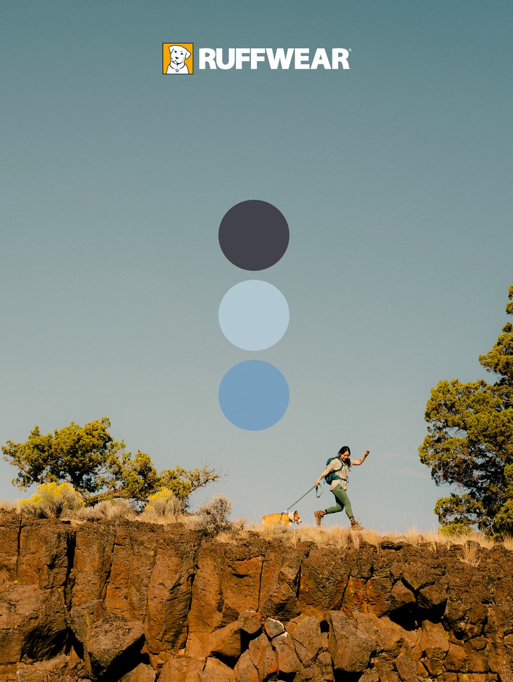 A dog human duo walk across a rocky edge together under a blue sky. Our blue collection shines bright.