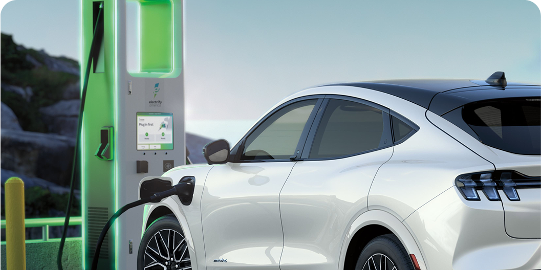 A white Ford vehicle charging at an illuminated green electric station