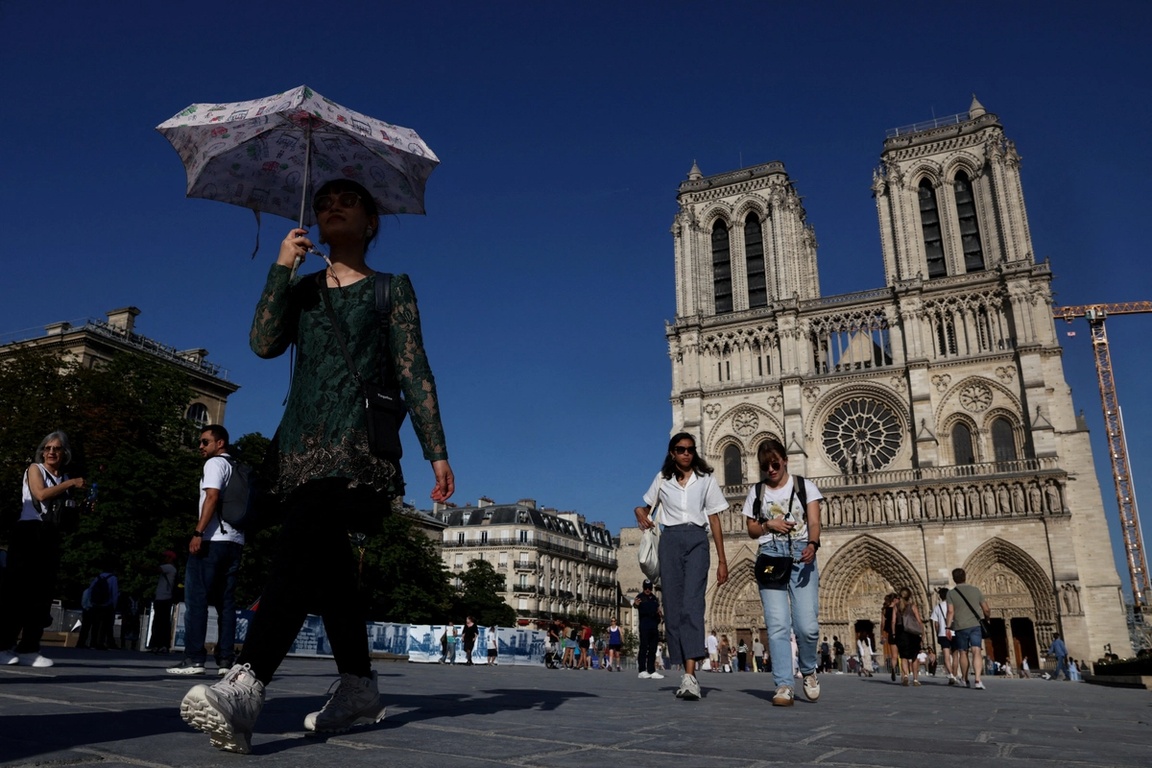  person shelters under an umbrella outside Notre-Dame Cathedral amid a severe heat wave 