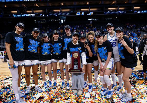 UCLA's women's basketball team pose for a photo in black T-shirts on a confetti-covered court floor