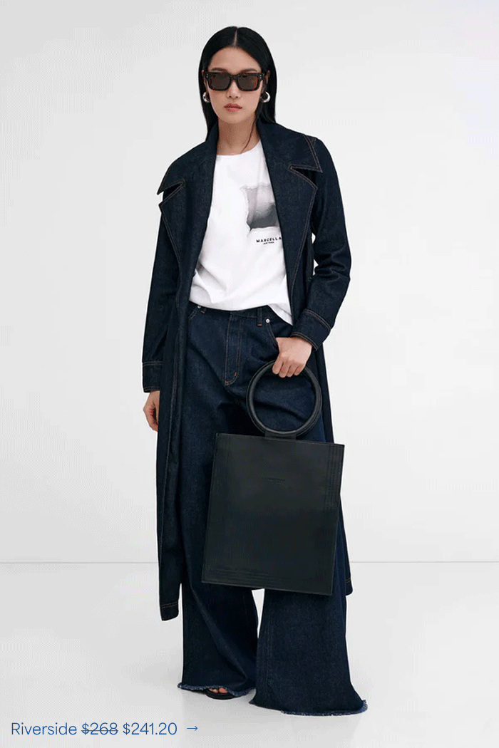 Xun wears The Riverside Trench Jacket over a white tee with wide-leg dark jeans in a white studio.