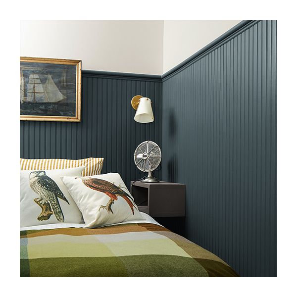 A bedroom with white upper walls and dark teal wainscoting features naval artwork, a bed with a checkered comforter, and throw pillows with birds on them.