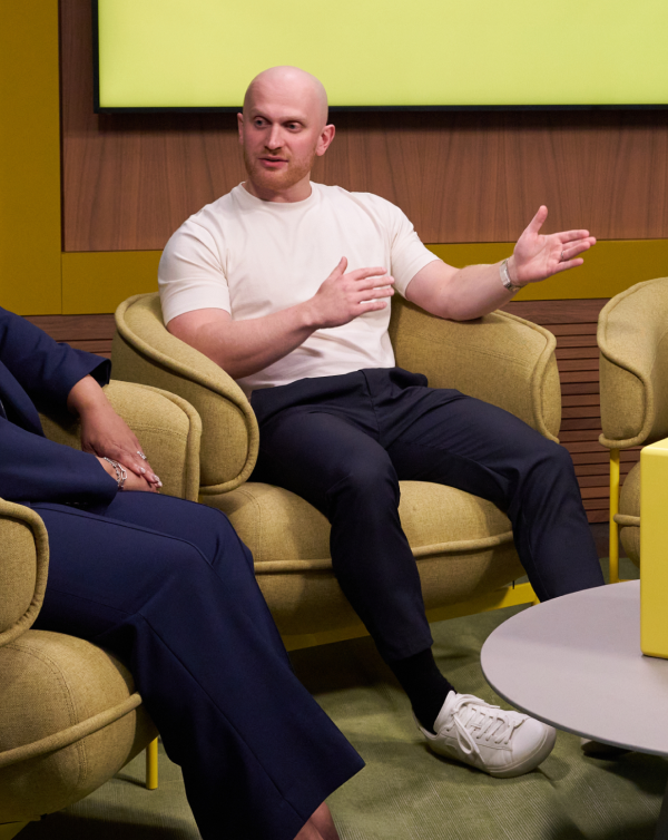 Speaker Anthony Bingham sits in a beige chair and talks to someone on his right. He is wearing a white shirt, black pants, and white sneakers. To the right, text reads, “What to expect,” “It takes just 1 hour a day to accelerate your marketing. Daily sessions near you are held 12-1 pm UTC-4.” There is a call to action button reading “Register now.””

To the right, speaker Tiffani Bova stands next to a yellow pedestal with the Intuit Mailchimp logo and a glass of water on it. She is wearing a navy blue blazer and a white shirt. 
