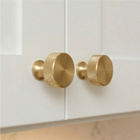 Two gold textured cabinet knobs on white doors.