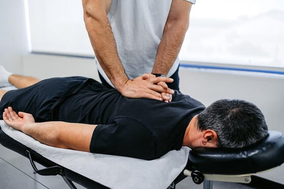 Chiropractor adjusting a client’s upper back while they lie face down.