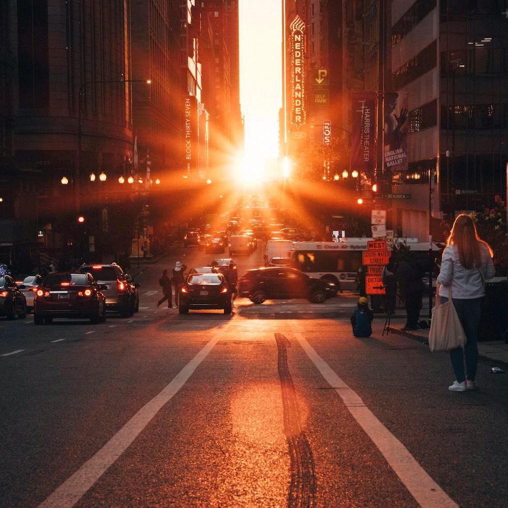 The sun shines through a gap between buildings in Manhattan, illuminating the street with orange light. 