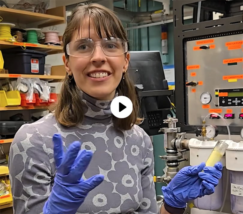 Katie Daehn wears protective goggles and gloves while holding a test tube.