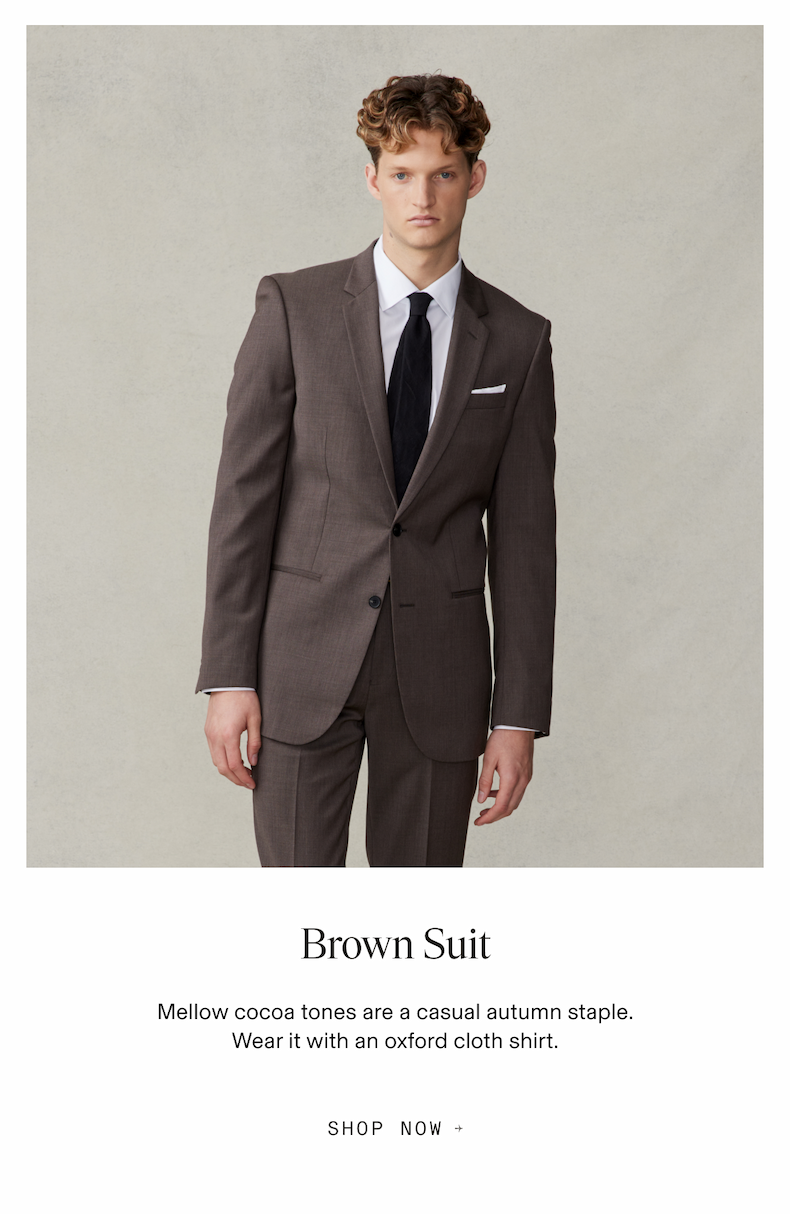 Model wearing a brown suit with white shirt and black tie. Text reads: Brown Suit. Mellow cocoa tones are a casual autumn staple. Wear it with an oxford cloth shirt. Button text: Shop Now.