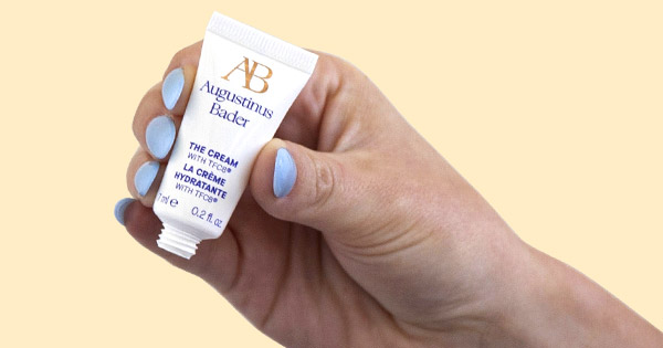 Woman squeezing travel-size Augustinus Bader The Cream on to her finger