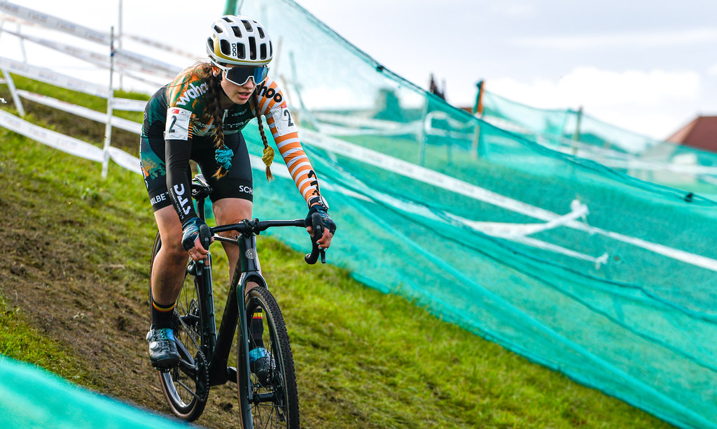 A cyclo-cross rider out of the saddle and pulling the brakes on a downhill grass section at a race.