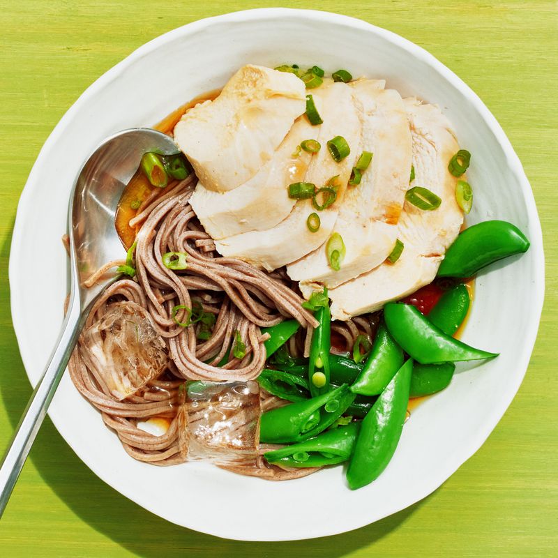 A bowl of boiled and sliced chicken breast, soba, snap peas, miso paste, lemon juice, and soy sauce topped with chopped scallions, sesame oil, and ice cubes.