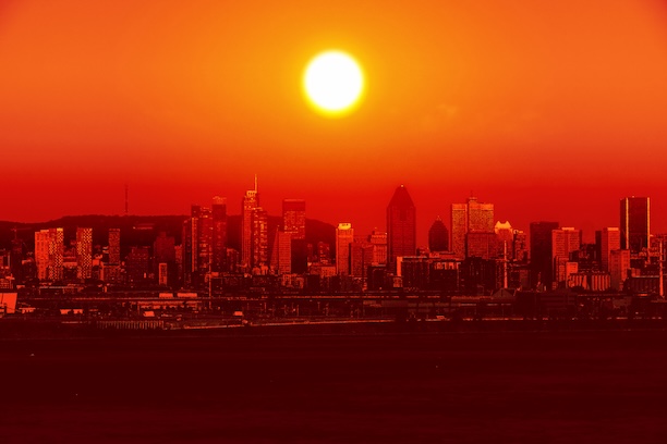 A city skyline tinted red and orange with the sun overhead to indicate extreme heat