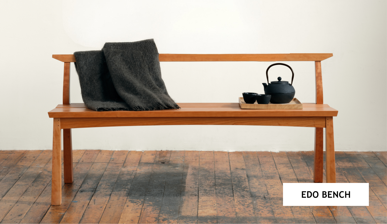 The Edo Bench in cherry with a blanket over the crest and a serving tray with a tea set on the seat. 