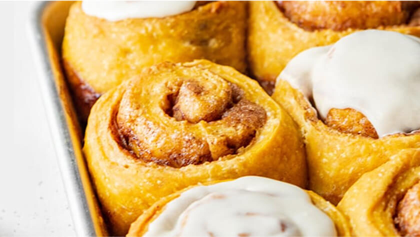 Zoomed-in image of a pan of cinnamon rolls. Some are frosted and some are unfrosted.
