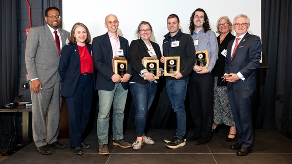 eight people lined up for photo, four in middle holding award plaques