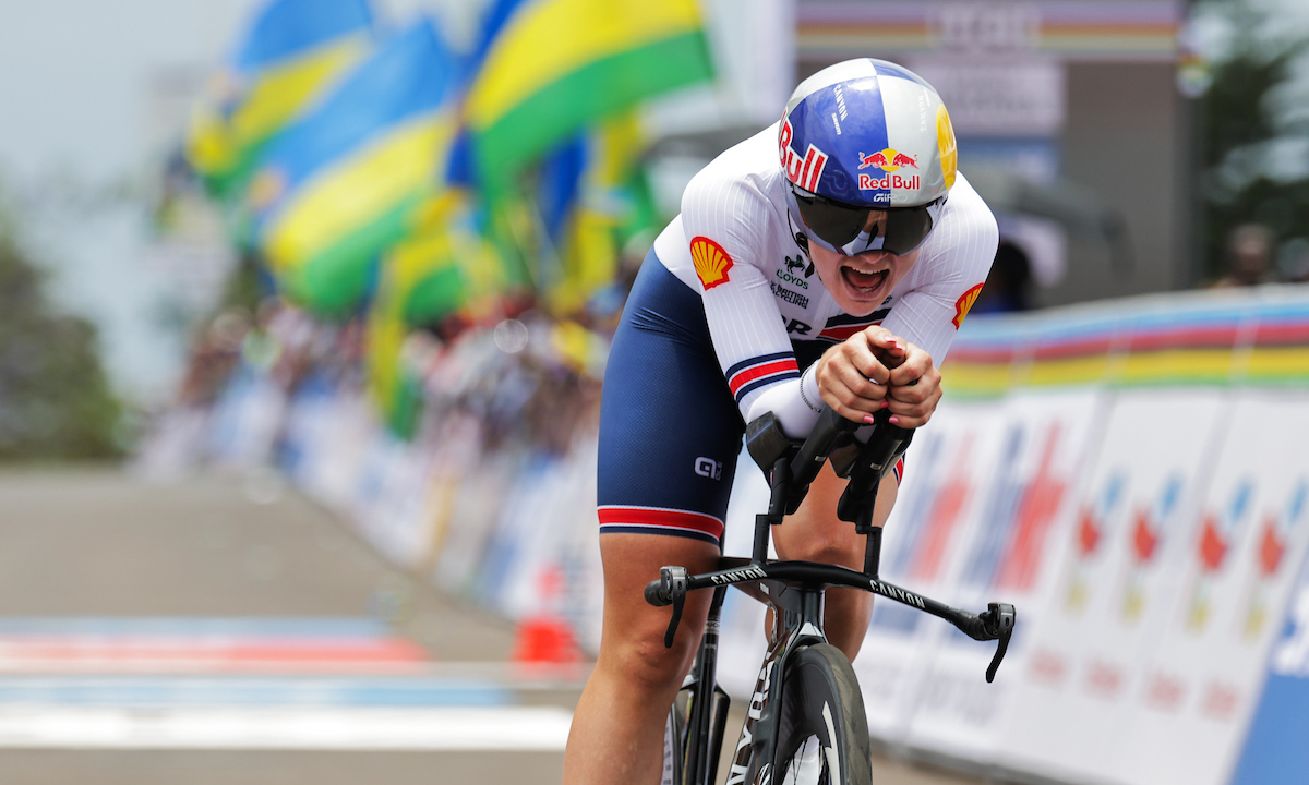 Zoe Backstedt on a time trial bike with Rwandan flags blurred in the background.