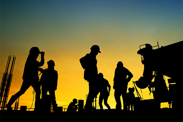 Shadowy silhouettes of construction workers against the backdrop of a setting sun. 