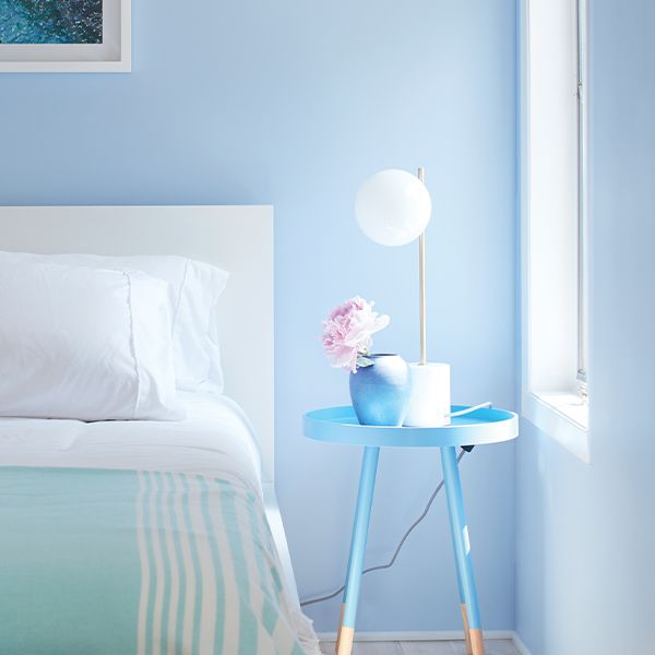 A blue-painted bedroom with blue and white bedding, light wood floors, and a blue night table.