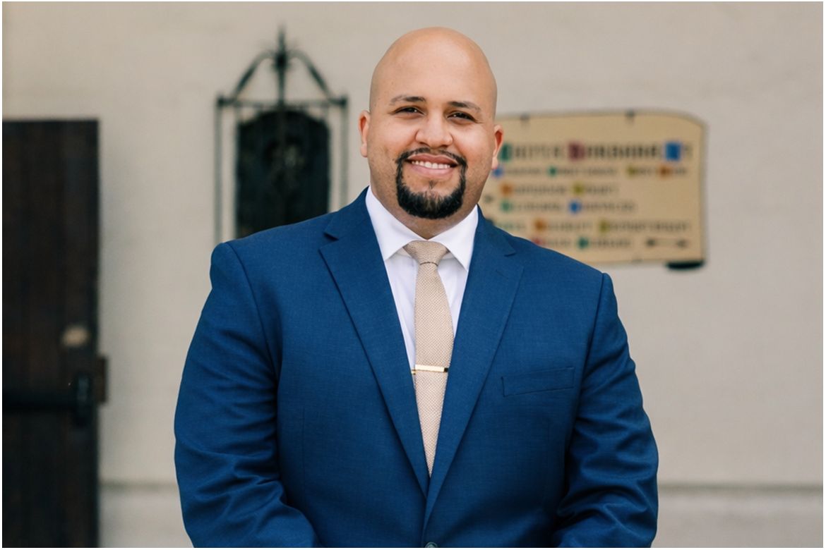 Midrange photo of Richard Mejia wearing dark blue suit and tan tie