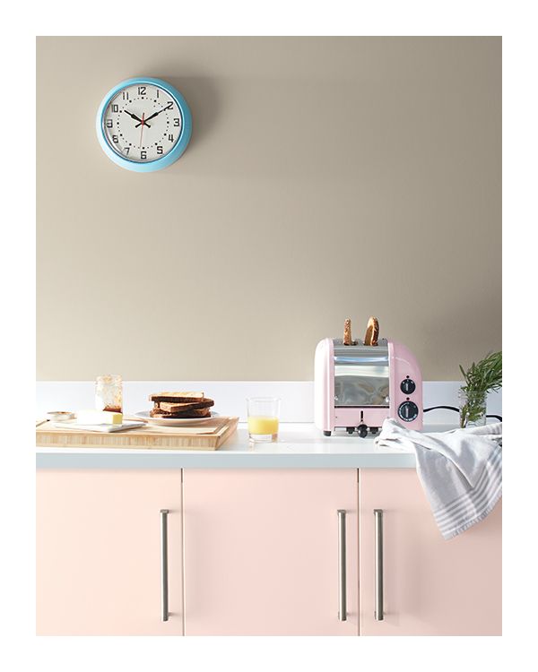 Light pink painted kitchen cabinets with a white countertop, against a tan wall.