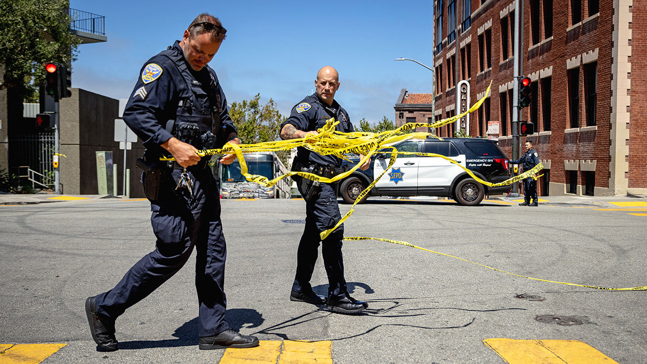 Two San Francisco Police Department officers remove tape at the scene of a shooting.