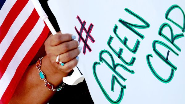 A demonstrator holds a small American flag and sign reading 'green card'.