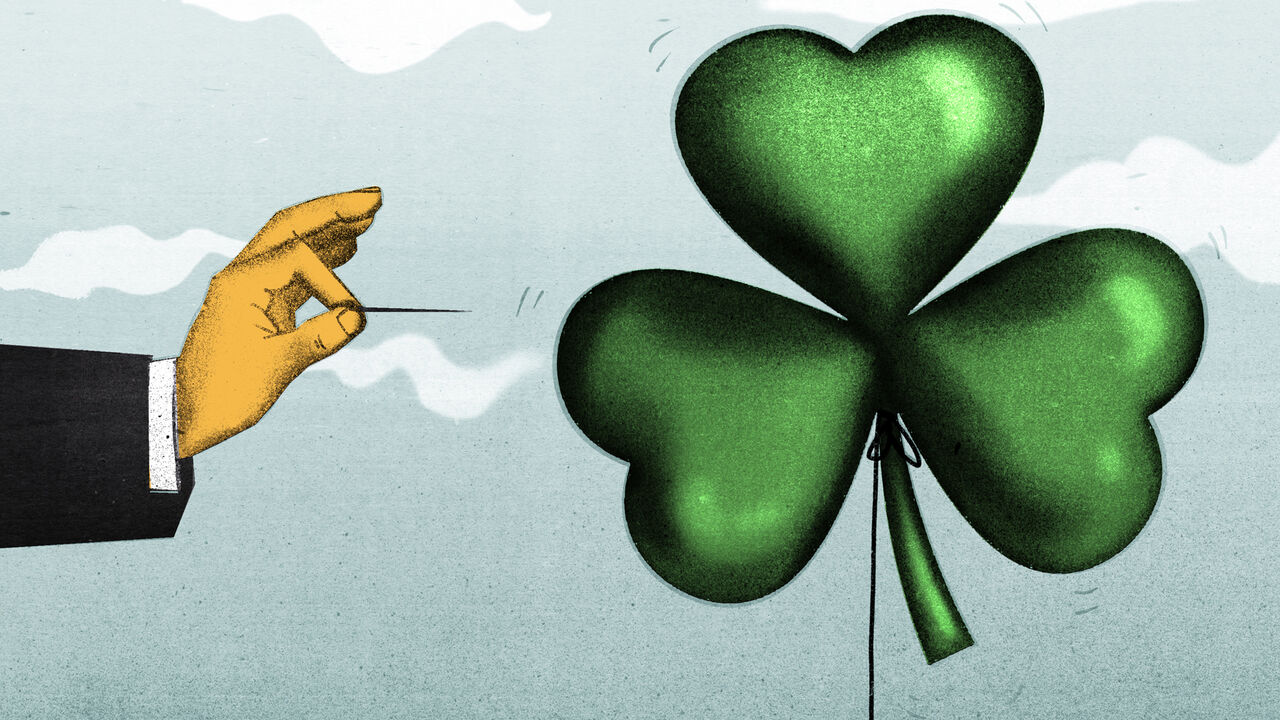 A hand with a pin is about to pop a balloon in the shape of a Shamrock
