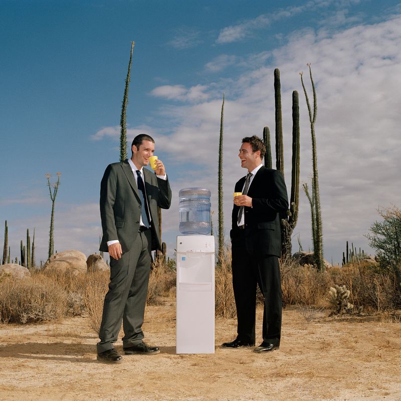 Two people standing next to water cooler in the desert.